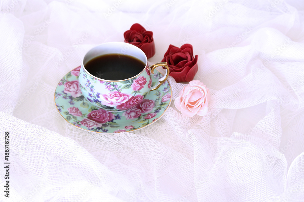 Morning hot coffe in mug and little red and pink flowers on white satin background. Closeup, top view. Seasonal, morning coffee, Sunday relax and still life concept. Free place for text