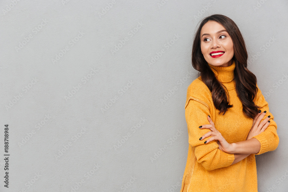 Obraz premium Pleased brunette woman in sweater with crossed arms looking away