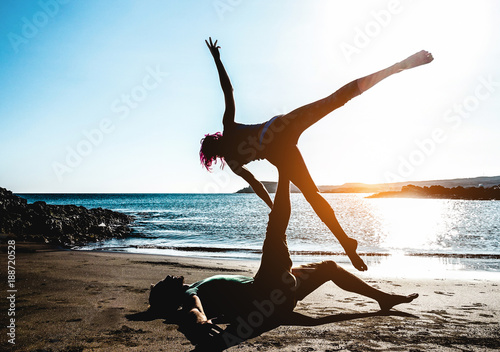 Fit young couple doing acro-yoga at sea beach. Man lying on concrete plates  and balancing woman on his feet. Beautiful pair practicing yoga together. -  a Royalty Free Stock Photo from Photocase