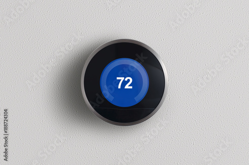 A simplistic photo of a round, modern, programmable digital thermostat in cooling mode, on a clean white wall.	 photo