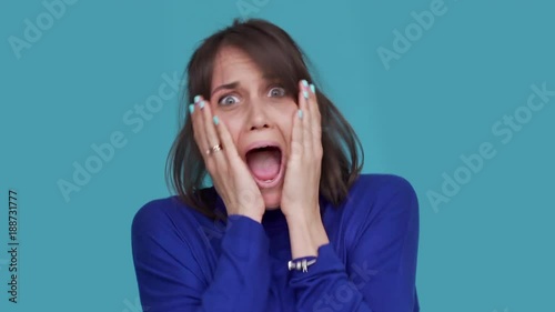 Portrait of lucky woman being ecstatic gesturing with hands clenching fists screaming in happiness acting like winner over blue background. Concept of emotions