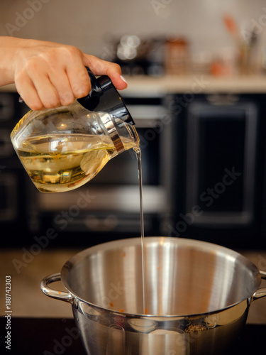 Female hand pouring olive oil in glass jag into a big metal bowl for making a dough. Home cooking on kitchen.