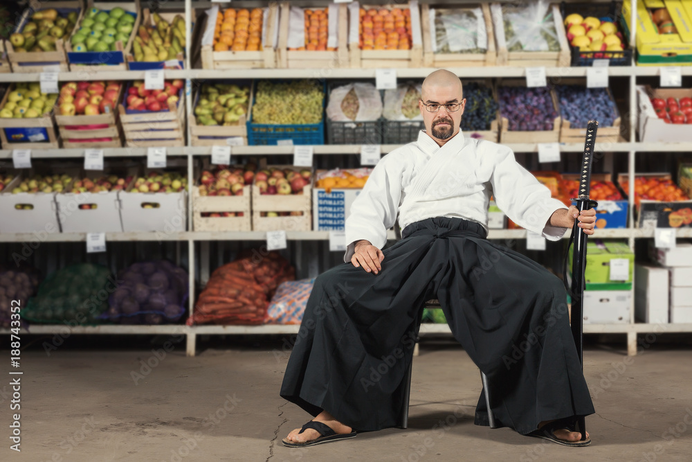 A man against the background with racks with fruits and vegetables dressed in Japanese kimono and hakama holding katana. Fruitarianism concept