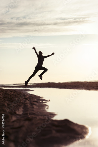 Emotions of young jumping girl silhouette in rays of sunlight at sunset.