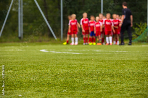 Youth Football Team with Coach on Pitch; Blurred Soccer Background. Soccer Training Session for Kids; Young Football Players Listening Coach Before the Training Match.
