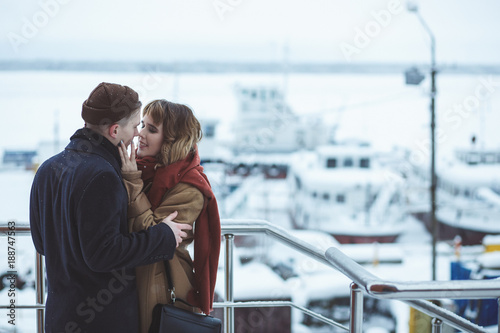 Young couple embracing at observation deck in winter city. Frozen ships in bokeh