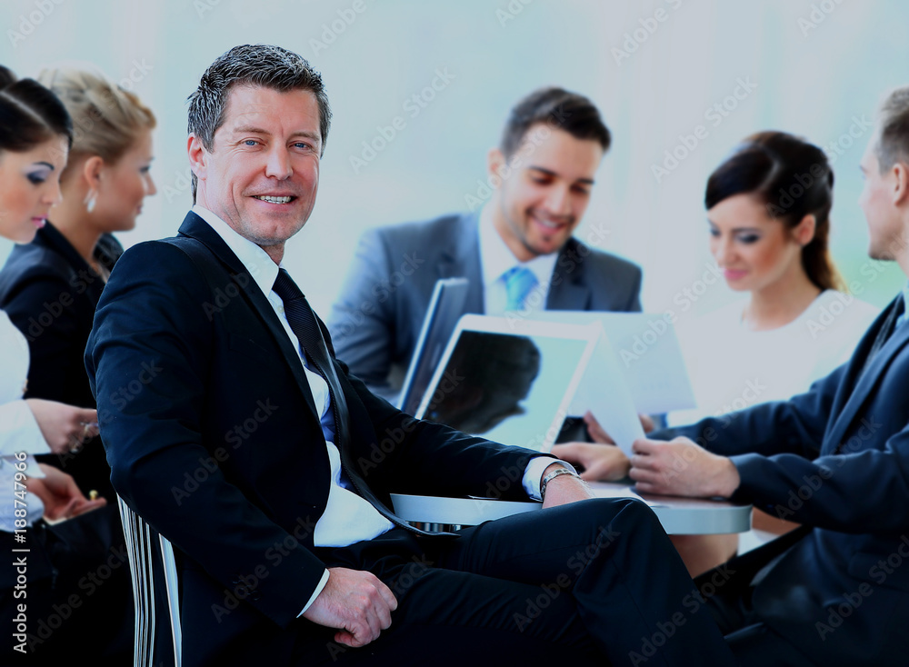 Portrait of mature business man smiling during meeting with colleagues in background. Portrait of mature business man smiling during meeting with colleagues in background.