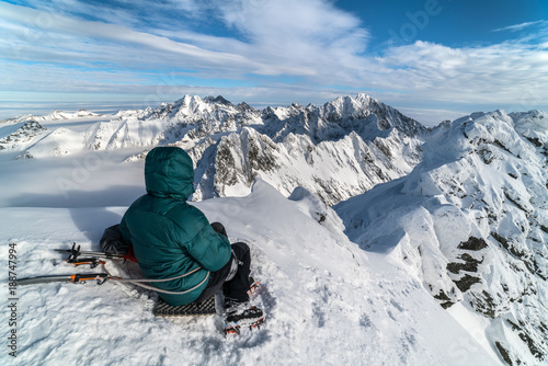 Young man sitting on summit in sunny day in winter snowy High Tatra mountains in Slovakia 