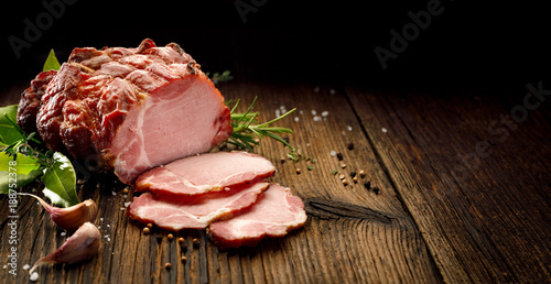 Sliced smoked gammon  on a wooden  table with addition of fresh  herbs and aromatic spices Fototapeta