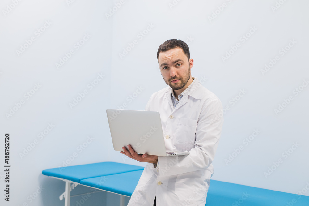 Minded successful doctor standing at his office and using laptop for his work Minded successful doctor standing at his office and using laptop for his work