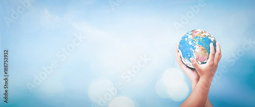 Earth Day concept: Two human hands holding earth globe over blurred blue sky background. Elements of this image furnished by NASA