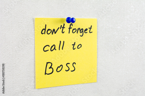 don't forget call to boss note reminder yellow sticker on a white wall pinned with blue pushpin, close up, selective focus