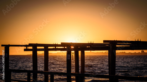 The sun sets over the horizon of Port Phillip Bay with a silhouetted wooden boat launch structure in the foreground. Melbourne Australia