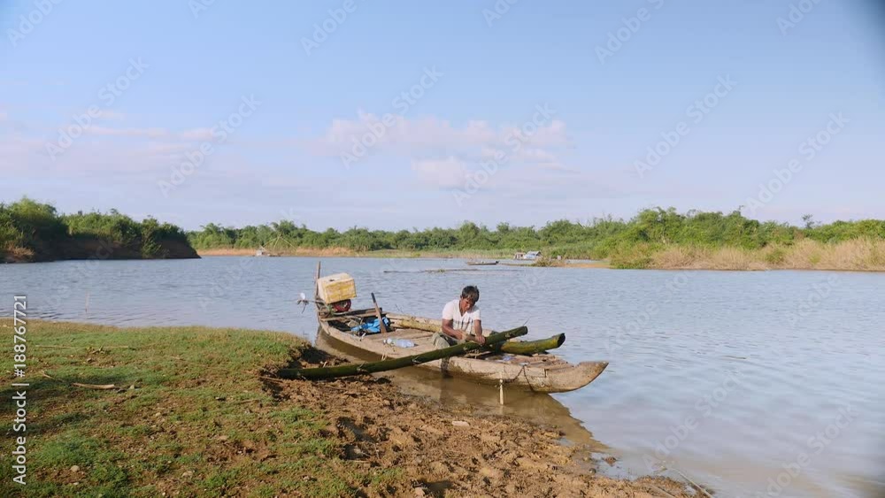 Man sawing bamboo stalks in a dugout canoe on the riverside