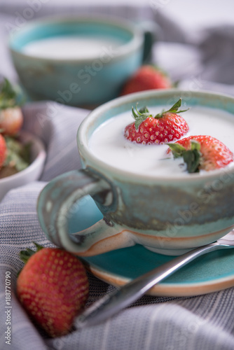 Fresh strawberries and cup of milk on a tablecloth.