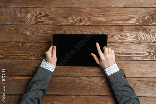 Top view of businesswoman sitting at wooden table and working with tablet