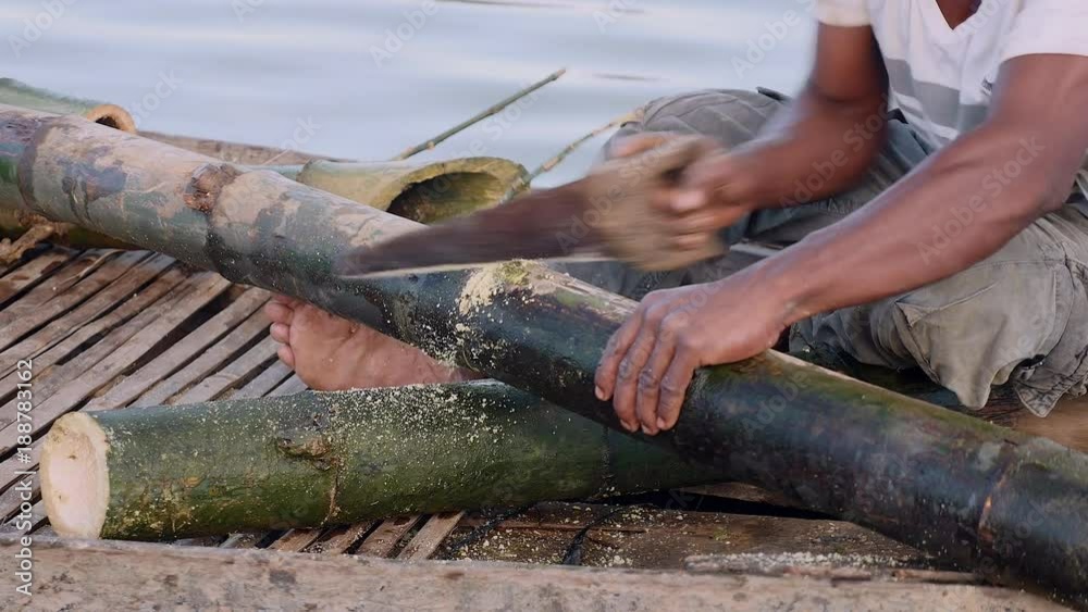 extreme close up on a man sawing bamboo stalk in a dugout canoe