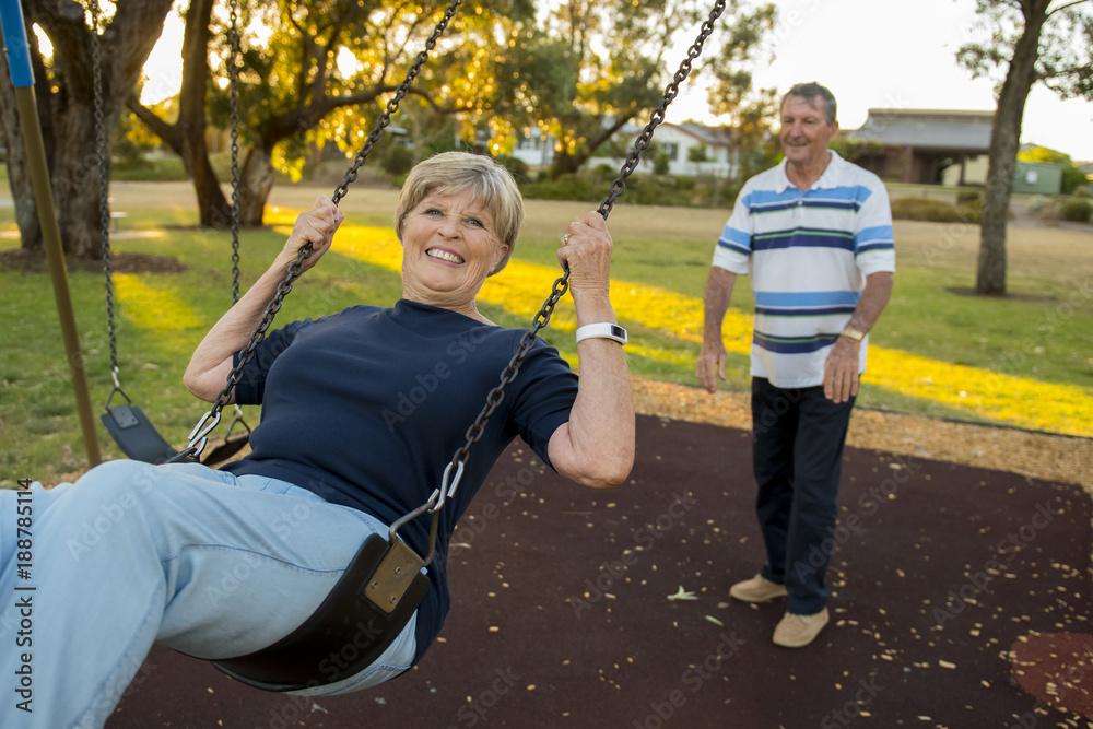 Obraz premium happy senior American couple around 70 years old enjoying at swing park with husband pushing wife smiling and having fun