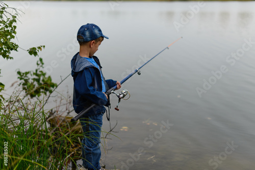 A fisherman boy on the river bank with a fishing rod in his hands. He wants to catch a big fish..