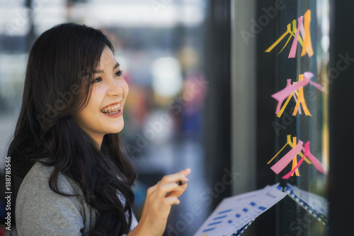 Business plan. Young female professional sticking colourful notes to a glass wall