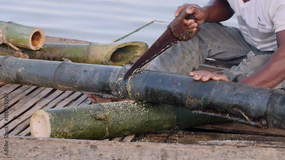 Close up on a man sawing bamboo stalk in a dugout canoe
