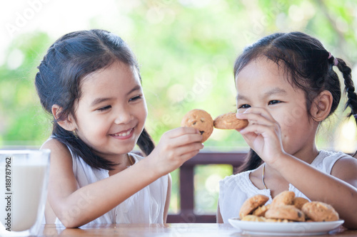 Two cute asian little child girls are eating cookies with milk for breakfast together with happiness