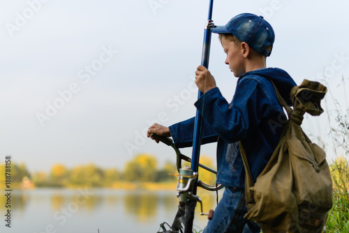 A fisherman boy on the river bank with a fishing rod in his hands. He wants to catch a big fish. He came by bicycle..