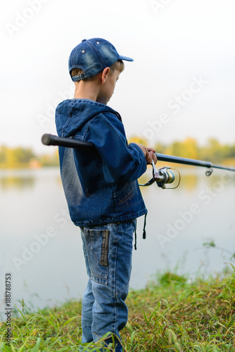 A fisherman boy on the river bank with a fishing rod in his hands. He wants to catch a big fish..