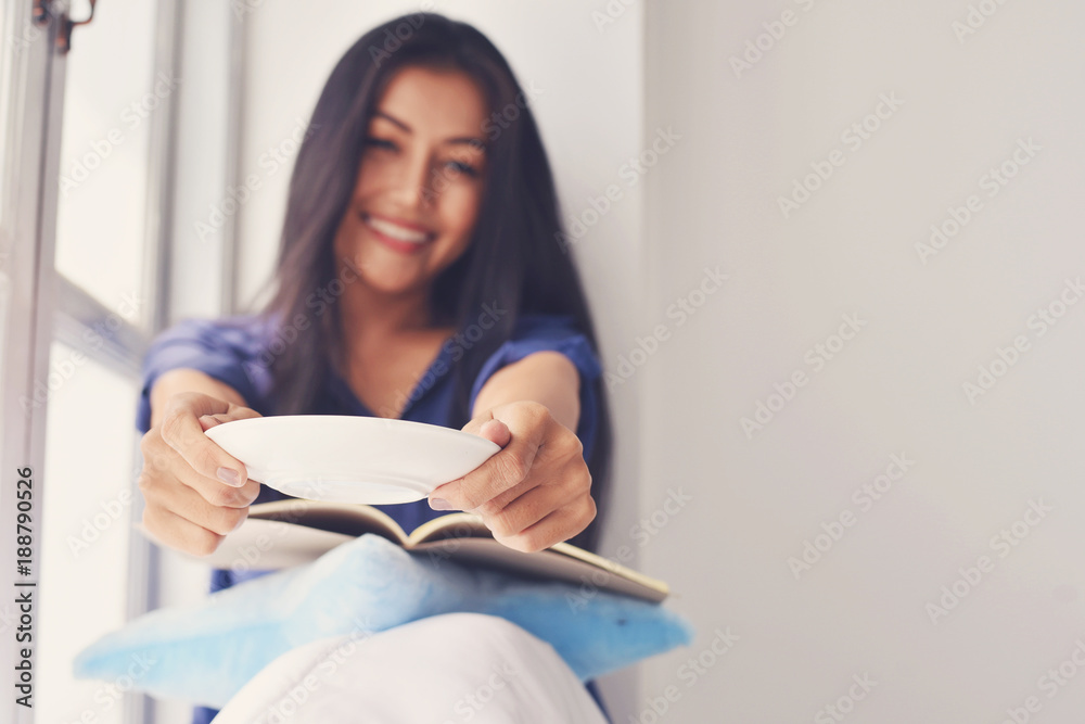 Women show empty plate after eating sweets and snacks during young woman reading a book at home, concepts of home and relaxing time Women show empty plate after eating sweets and snacks during young woman reading a book at home, concepts of home and relaxing time