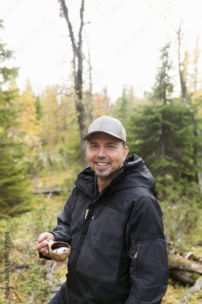 Smiling man standing in forest with water in wooden mug Smiling man standing in forest with water in wooden mug