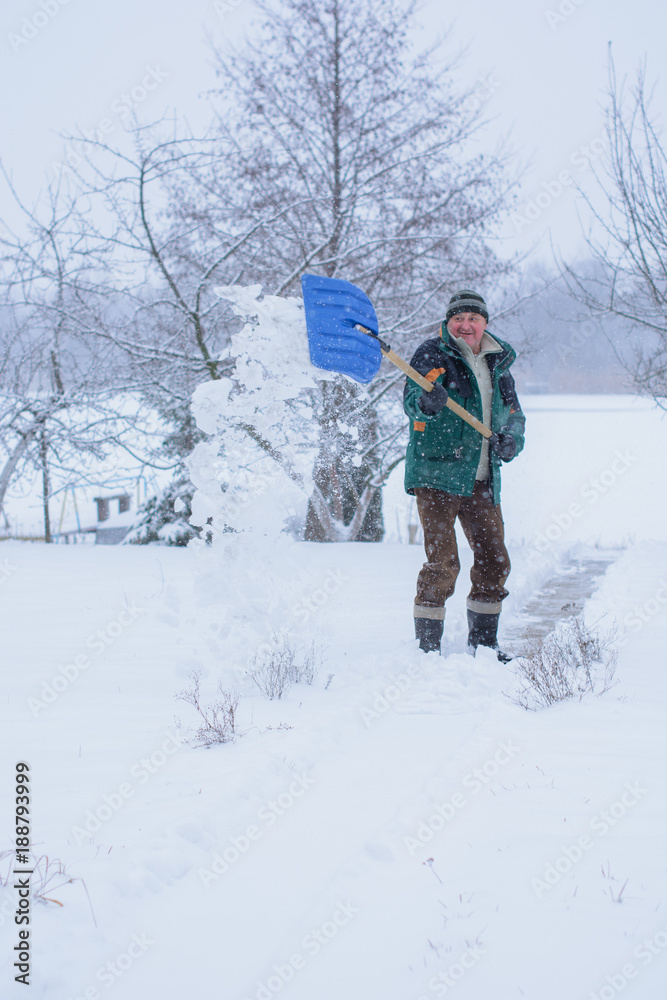 Mature man cleans the snow with a shovel near his house. Difficulties of weather conditions during life in a private house and countryside 