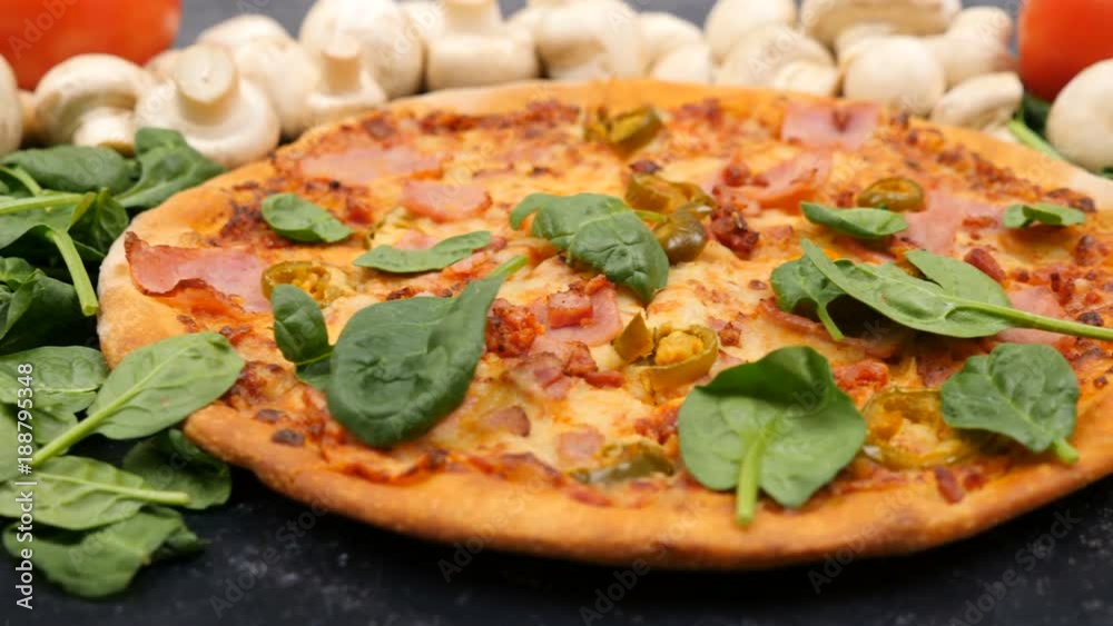 Leaves of baby spinach falling on fresh baked pizza lying on dark wooden background Leaves of baby spinach falling on fresh baked pizza lying on dark wooden background