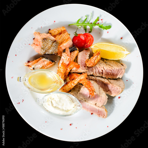 Appetizing Tuna steak with tomato, lemon and sauce in a white plate isolated on black background. Top view, flat lay