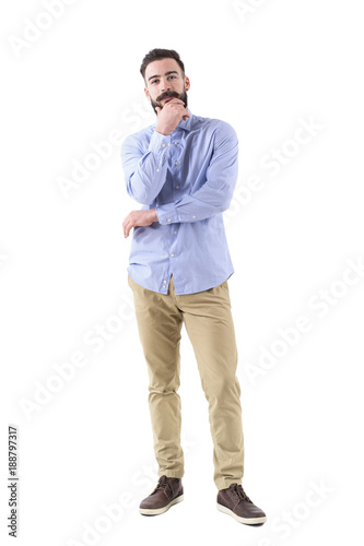 Bearded business man thinking with hand touching beard looks at camera. Full body length portrait isolated on white studio background. 