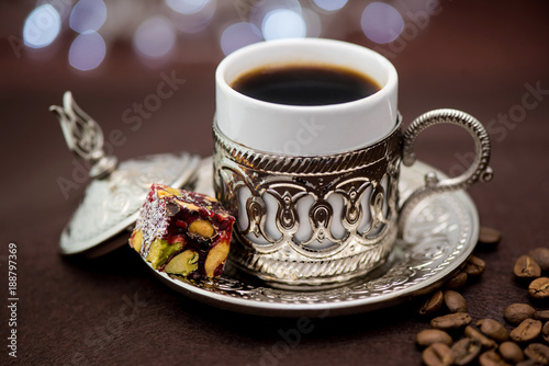Traditional Turkish coffee in traditional metal cup on brown background with Turkish delight and bokeh photo