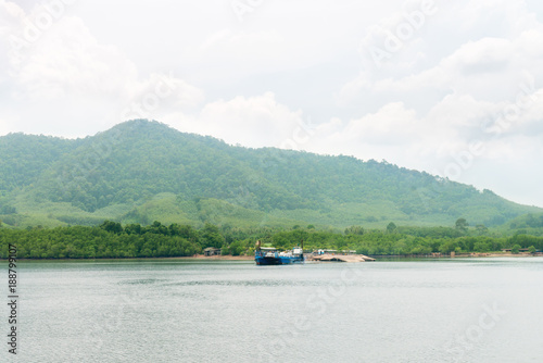 Green hilly tropical island with blue ferry in the sea