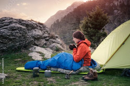 Female traveler in sleeping bag near the tent in mountains, Turkey