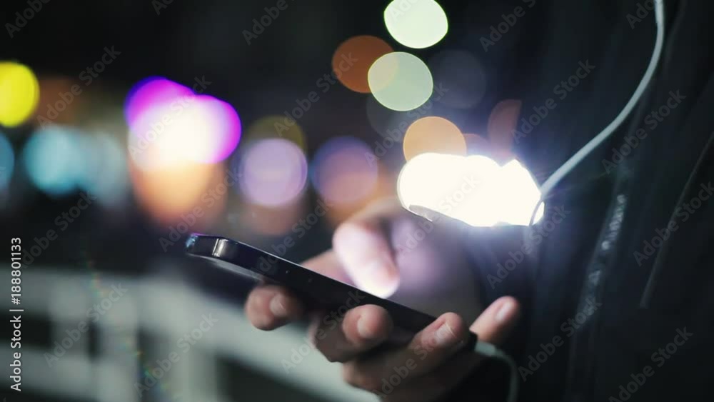 An arty closeup of male hands touching the screen of his mobile and seeking some info on a city street with bkurred lights in the evening An arty closeup of male hands touching the screen of his mobile and seeking some info on a city street with bkurred lights in the evening