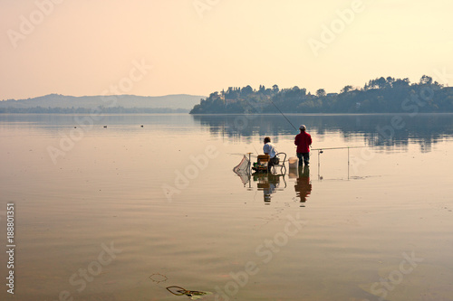 Two fishermen, immersed in the tranquil waters of a lake, are dedicated to sport fishing on a quiet summer afternoon