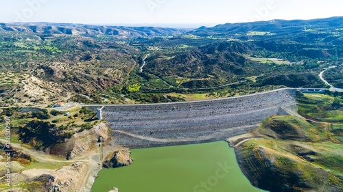 Aerial bird eye view of Kalavasos rockfill dam wall, Larnaca, Cyprus. The street bridge over the reservoir crossing Vasilikos river and the hills around the water from above.