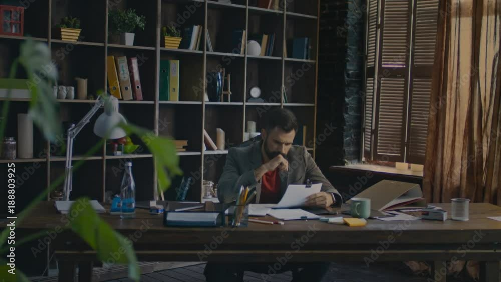 Serious business man reading documents at table. Young businessman signing documents at home office. Paperwork in creative studio. Business owner doing paper work