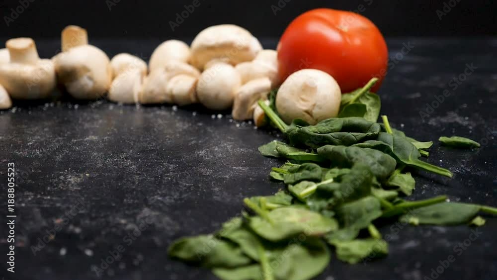 Slow motion on delicious pizza falling on dark wooden background surrounded by mushrooms, spinach and tomatoes