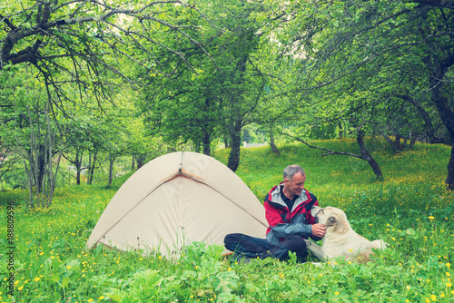 Joyful traveler plays with large shepherd dog next to the tent