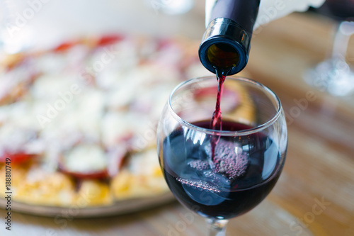 Valokuva Red wine is poured from the bottle into the glass in the restaurant or cafe, in the background there is a silhouette of pizza