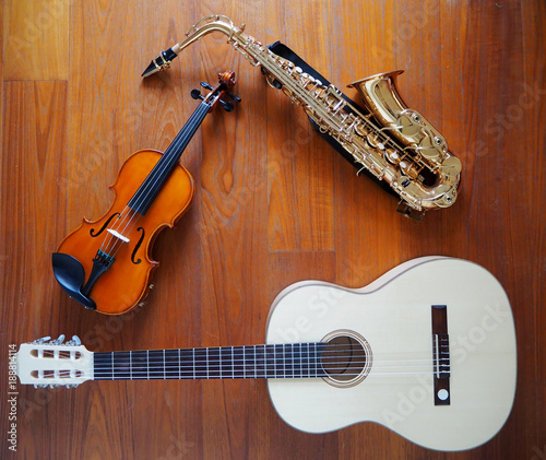 A violin, a guitar and a saxophone leaning together. Teak wood background.