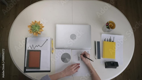 Business woman working with a business graph and a laptop that stands on a white table. Top view. Hands close up