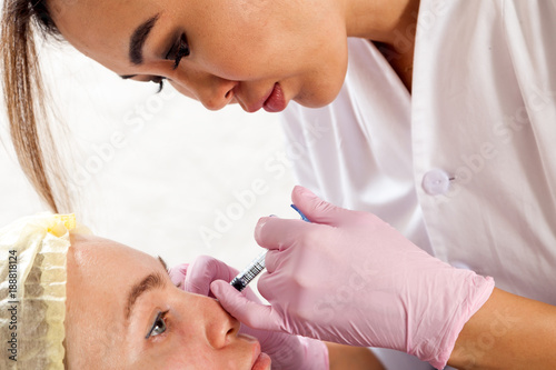 Close-up of a dark-haired woman asian beautician injects an injection of Botox into the cheekbones of a young woman to correct the shape