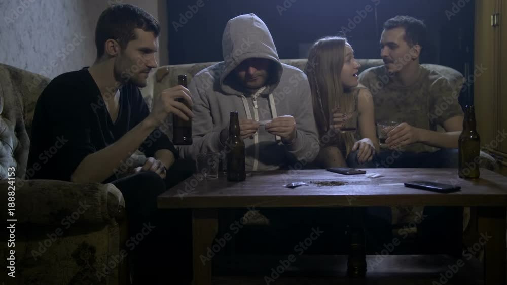 Four young alcoholics sitting on sofa at night in domestic room at home ...