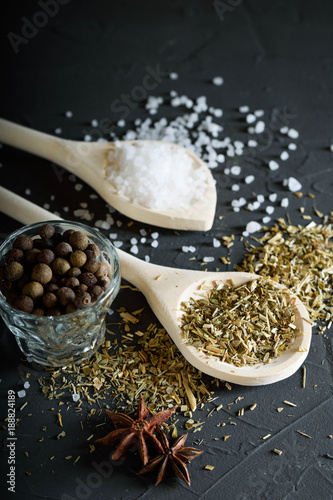  Wooden spoon with Italian seasoning - dried oregano with thyme, basil and vegetables .Oregano in a wooden spoon on a rocky concrete dark black background with a place for text Top view. A wooden spoo