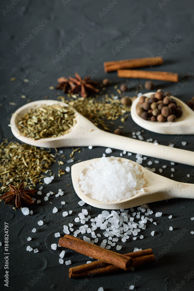 Fototapeta premium Wooden spoon with Italian seasoning-dried oregano with thyme, basil and vegetables.Oregano in a wooden spoon on a rocky concrete dark black background with a place for text.Top view.salt crystals pep